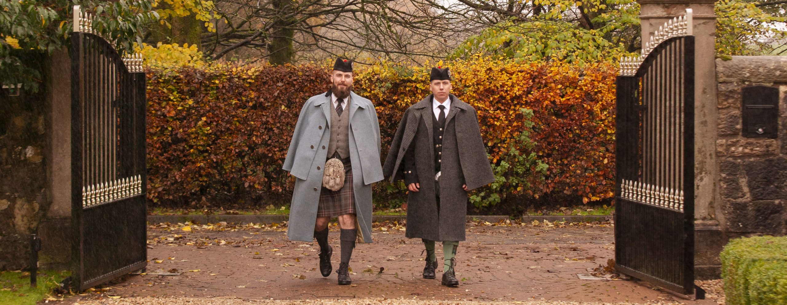 2 people walking in front of gates wearing tweed capes