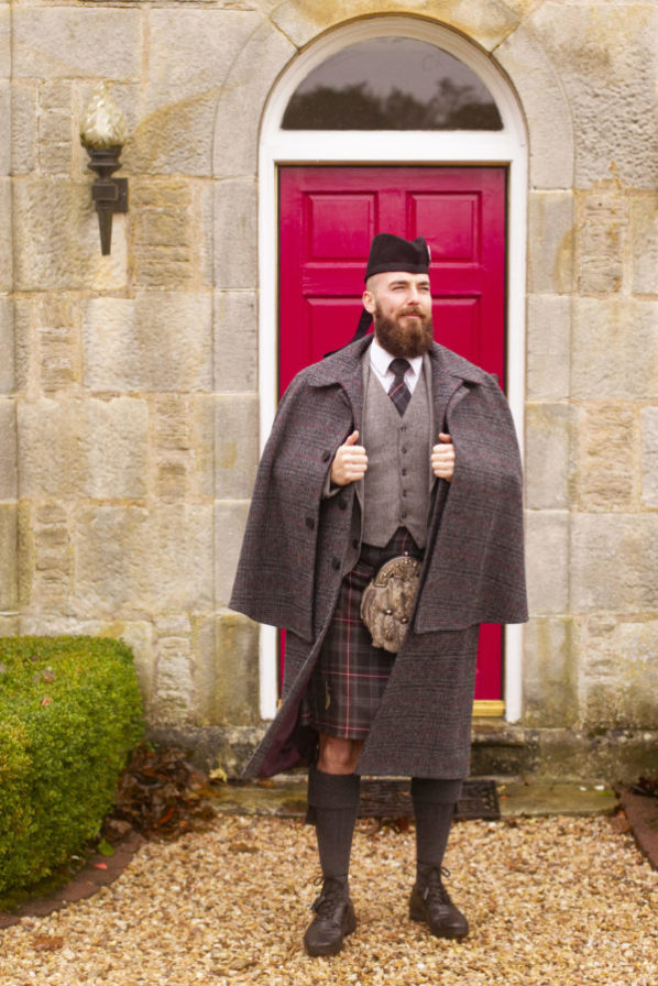 Person in a tweed cape in front of a red door